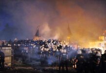 Turkey Locks Down Capital Before NATO Leaders Arrive A large crowd of police officers in helmets facing a smoky protest scene at night