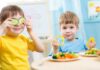 Two children playing with vegetables while enjoying a meal