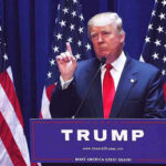 “Nobody Can Be Like Us”: Trump’s Boldest America 250 Message Yet Man speaking at podium with USA flags behind him.