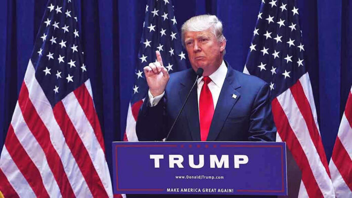 1456399979 Man speaking at podium with USA flags behind him.