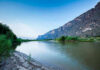 Mystery Plague: Doctors Stumped as Mystery Illness Hits River with mountains and greenery in the background.