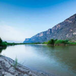 Mystery Plague: Doctors Stumped as Mystery Illness Hits River with mountains and greenery in the background.