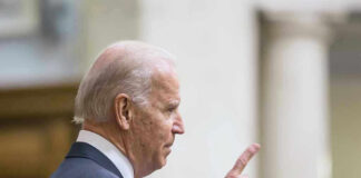Man in suit pointing while speaking at podium.