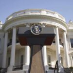 Press podium with presidential seal in front of the White House
