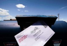 Mail-in ballot being inserted into a blue USPS mailbox