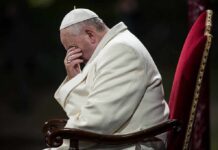 Pope sitting with his head bowed and hand covering his face