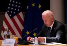 Pressure, Diplomacy, and No Clear Endgame elderly man at conference table with flags in background