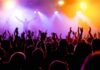 Crowd at a concert with raised hands and colorful stage lights