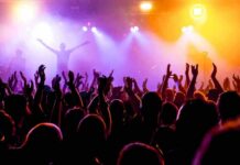 Crowd at a concert with raised hands and colorful stage lights