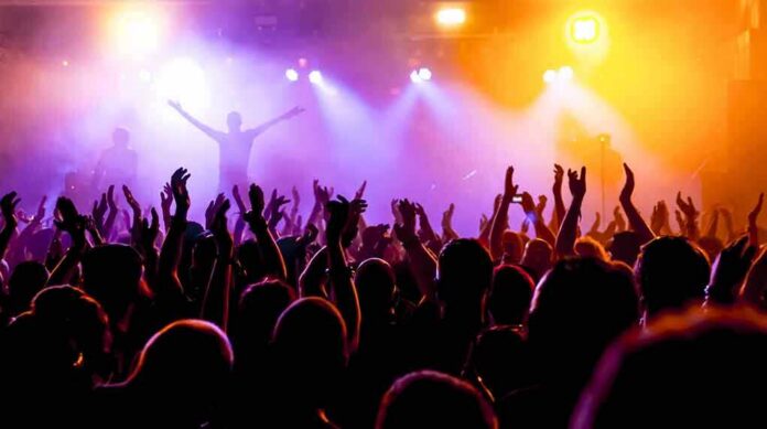 shutterstock_214402048 Crowd at a concert with raised hands and colorful stage lights