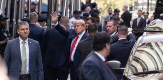 Man in suit waves while surrounded by security detail on a city street