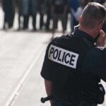 Cops Doubt: Teen’s Final Pleas Captured on Bodycam Police officer in uniform communicating with a crowd in an urban setting