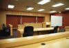 Interior view of an empty courtroom with wooden furniture and American flags