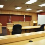 One Vacation. Three Lives Lost. Interior view of an empty courtroom with wooden furniture and American flags