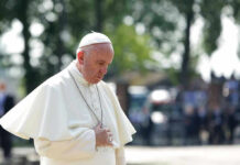 Bishops’ Ritual Appearance Sparks Outrage Man in white religious attire looking down thoughtfully.