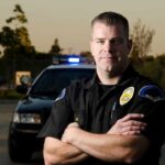 Officer’s Gun Targeted in Shocking Virginia Incident police officer standing with arms crossed in front of patrol car