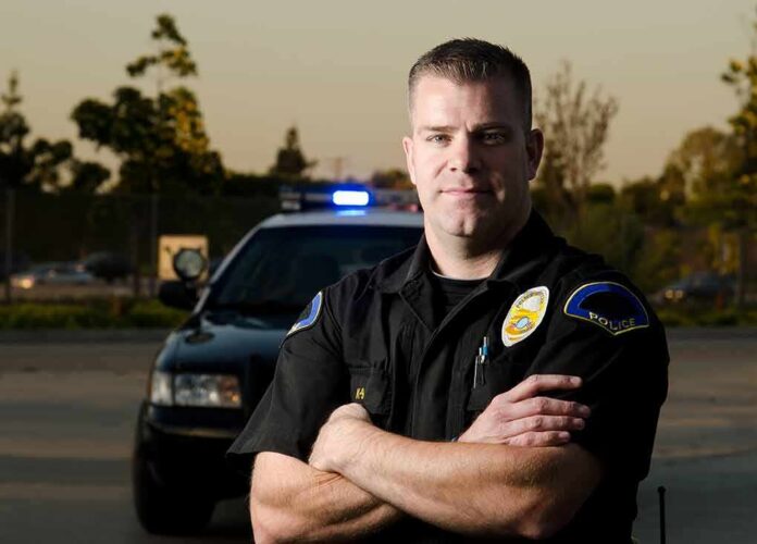shutterstock_135974135 police officer standing with arms crossed in front of patrol car