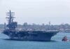 Aircraft carrier escorted by a tugboat in a harbor