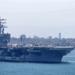 No Factory. No Port. The Navy Built Drones at Sea. Aircraft carrier escorted by a tugboat in a harbor
