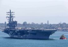 No Factory. No Port. The Navy Built Drones at Sea. Aircraft carrier escorted by a tugboat in a harbor