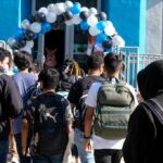 Students with backpacks enter a school under a balloon arch