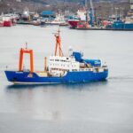 One Giant Shark. One Old Nuclear Mystery. Blue research vessel in harbor with orange cranes