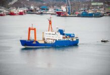 One Giant Shark. One Old Nuclear Mystery. Blue research vessel in harbor with orange cranes