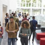 Trust Crash Hits Colleges Again Students walking through a bright campus atrium using mobile devices