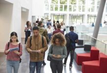 Trust Crash Hits Colleges Again Students walking through a bright campus atrium using mobile devices