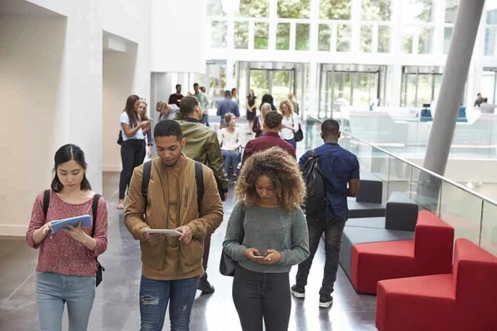 shutterstock_478513882 Students walking through a bright campus atrium using mobile devices