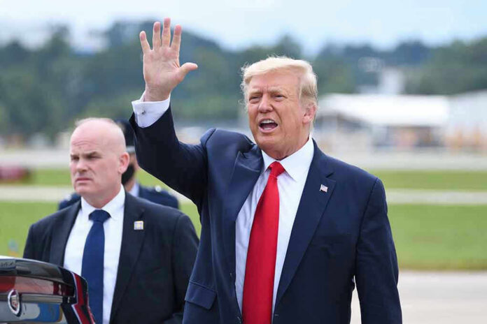 Donald Trump waves while walking outdoors with security nearby