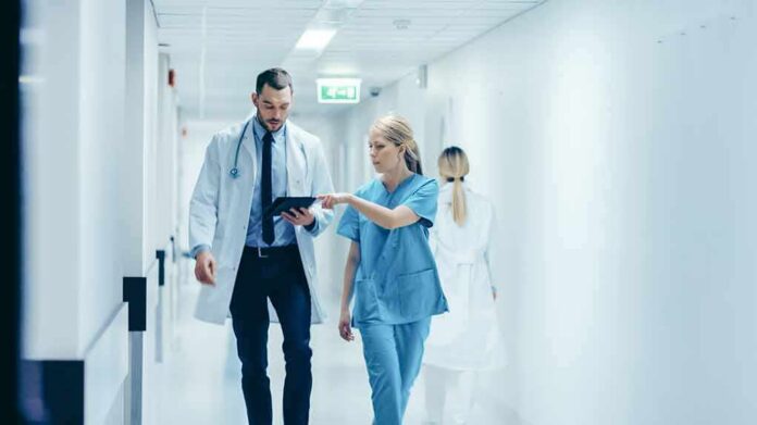 shutterstock_1189798168 Doctor and nurse walking in a hospital corridor reviewing a tablet