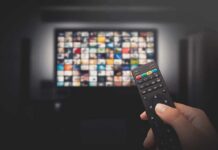 Hand holding TV remote toward a screen with streaming thumbnails