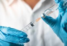 Gloved hands drawing liquid into a syringe from a vial