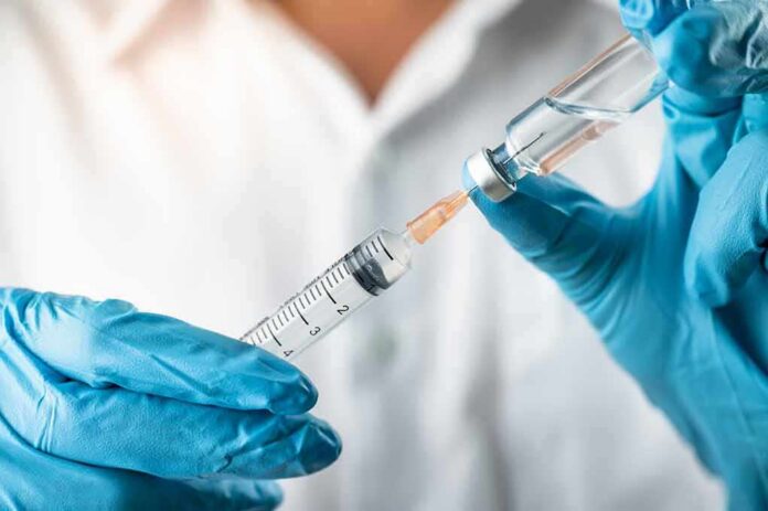 Gloved hands drawing liquid into a syringe from a vial