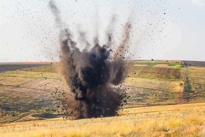shutterstock_156172331-1 Explosion sending dark smoke and debris into the air in an open field