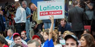 Child holding a 'Latinos for Trump' sign at a crowded rally