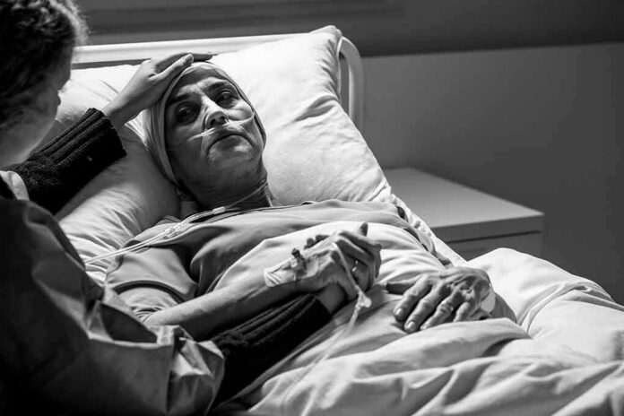 shutterstock_1677368530-1 Patient in hospital bed with nasal oxygen held by visitor