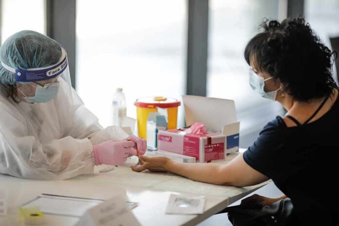 Healthcare worker performs finger-prick test on masked patient