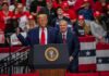 Trump Rejects AI Pause Backed by Sanders two men at a podium during a large indoor rally