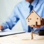 Hand holding a wooden house model with keys