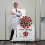 Cardboard cutout of doctor with COVID-19 virus info display