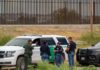 16 Months of Zero Border Releases law enforcement officers confer beside patrol vehicles near a border fence