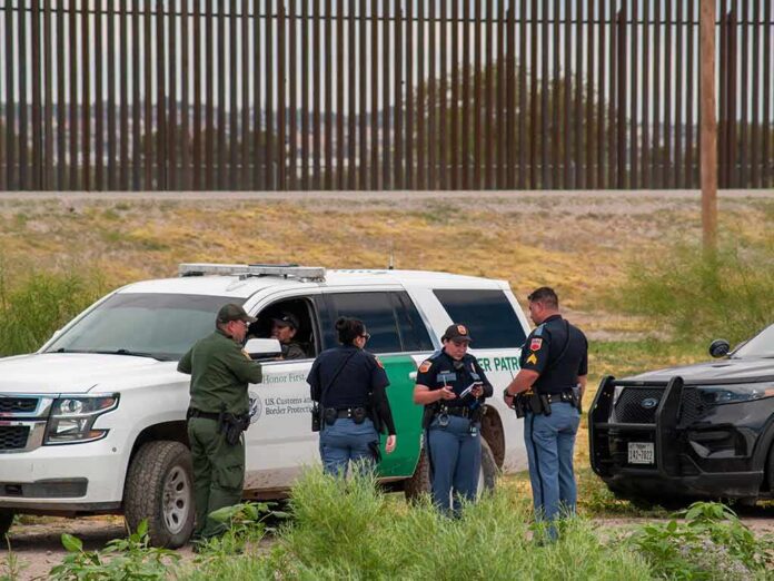 shutterstock_2015745392-1 law enforcement officers confer beside patrol vehicles near a border fence