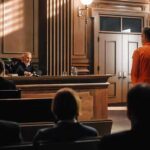 Defendant in orange jumpsuit stands before judge in courtroom