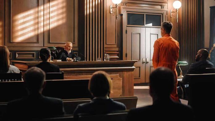 Defendant in orange jumpsuit stands before judge in courtroom