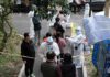 Christian Jones and others wait at an outdoor COVID-19 testing site with staff in protective suits