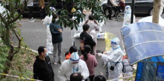 Christian Jones and others wait at an outdoor COVID-19 testing site with staff in protective suits