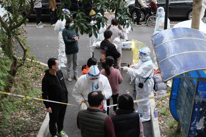 Christian Jones and others wait at an outdoor COVID-19 testing site with staff in protective suits