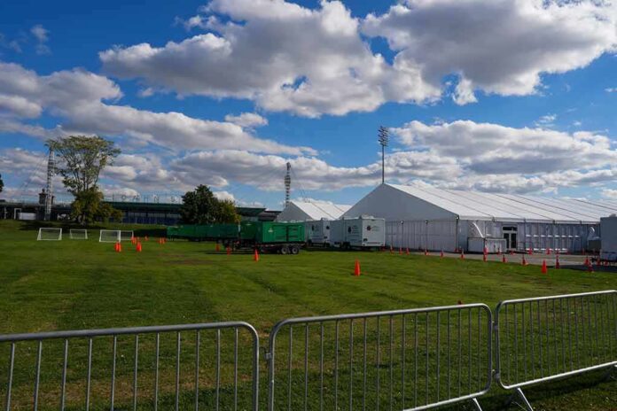 Temporary white tents and equipment on a grassy field with traffic cones and metal barriers